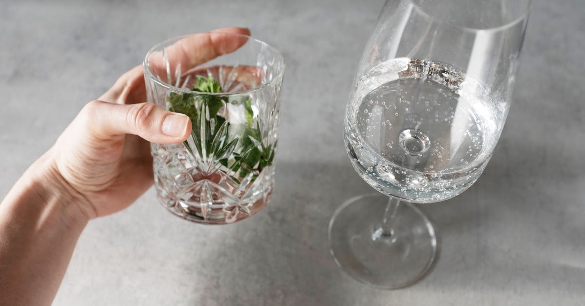 Homemade sauerkraut liquid level below cabbage. Should I add brine? - Crop person holding glass with herbs and water near wineglass with tonic on gray table