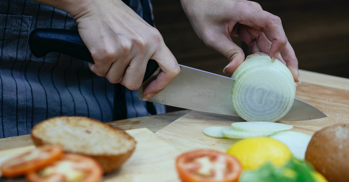 Horizontal cuts when dicing an onion - Unrecognizable female cook slicing onion on cutting board at table with blurred tomatoes and toasted buns in kitchen during cooking process