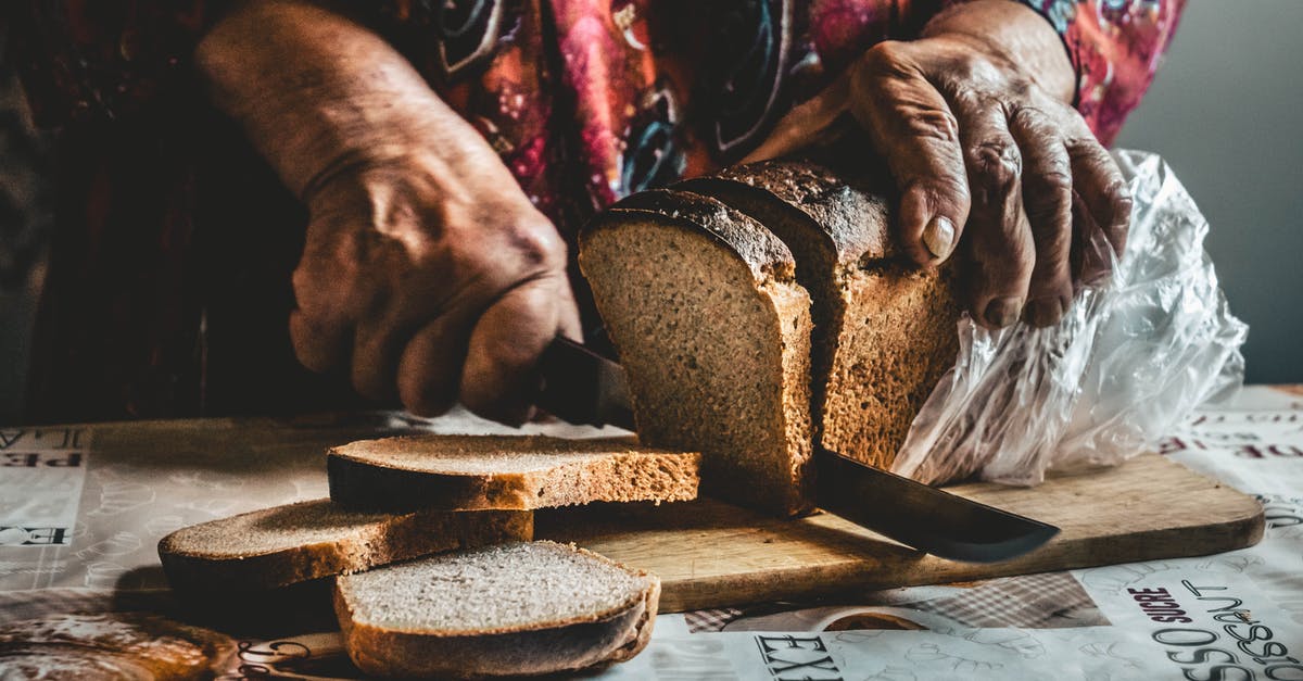 How and when should I use a bread knife? - Close-Up Shot of a Person Slicing a Bread on a Wooden Chopping Board