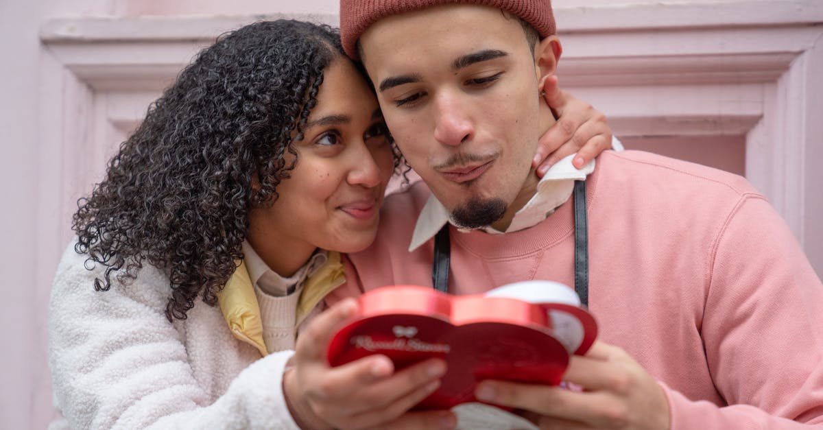 How are you supposed to eat ribbon candy? - Joyful young ethnic couple embracing and eating yummy candies from heart shaped gift box during anniversary celebration