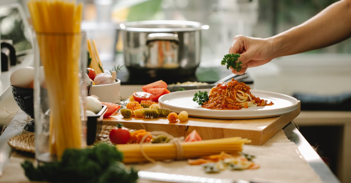 How can I add meat into a completed tomato sauce? - Crop anonymous chef adding parsley to spaghetti with tomato and meat while cooking lunch in kitchen