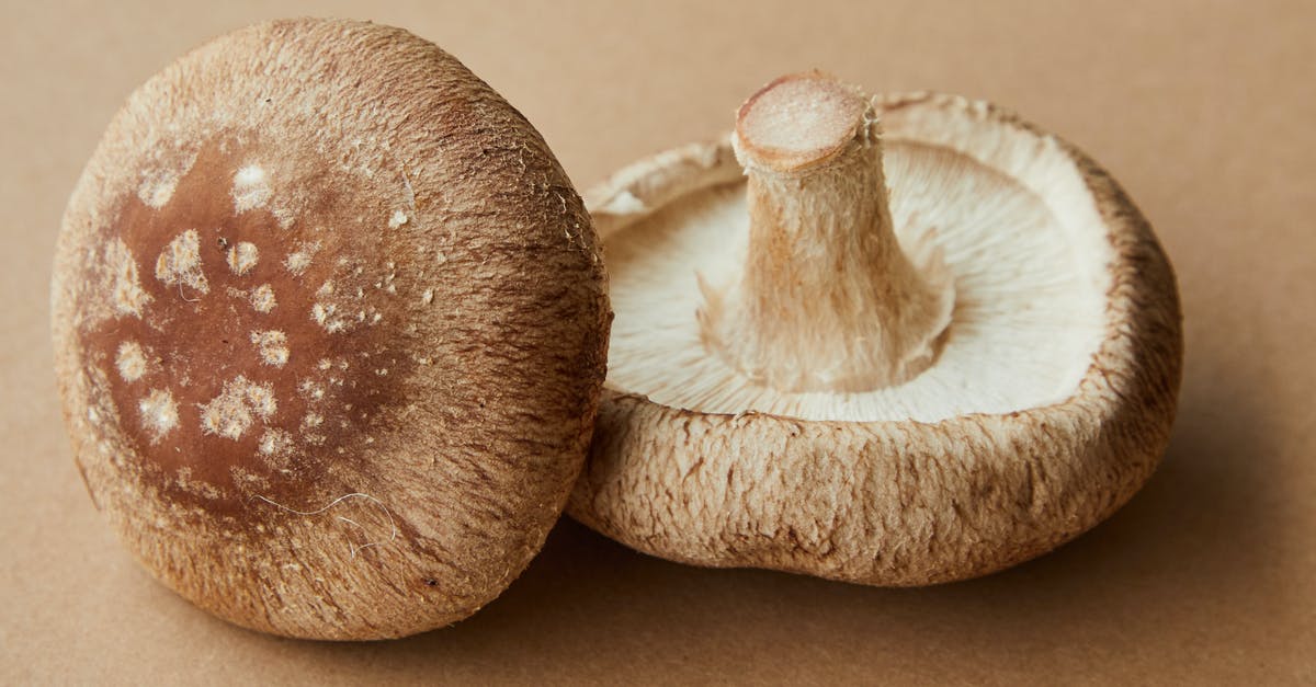 How can I avoid from turning mushrooms brown while freezing it? - High angle of delicious raw mushrooms with spotted caps placed on light brown background