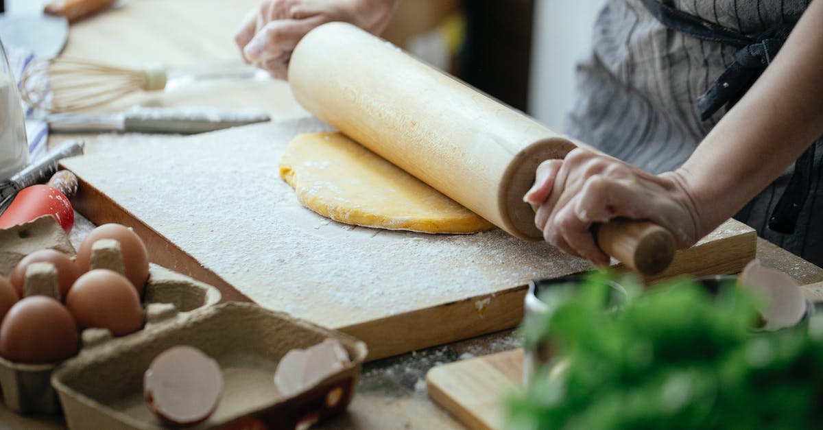 How can I buy or make pasteurized eggs? - Unrecognizable female cook flattening dough with rolling pin while standing at table with wooden board against blurred background in kitchen