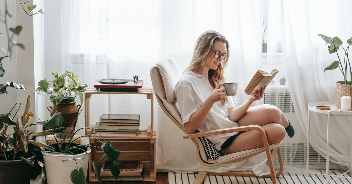 How can I chill ice coffee quickly? - Cheerful young female in eyeglasses with cup of beverage reading textbook in armchair between potted plants in house room