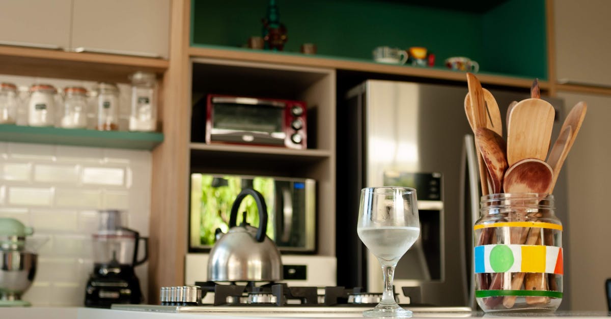 How can I clean my stainless steel teapot? - Glass of cold water and wooden utensils in jar placed on counter near stove with kettle in cozy kitchen with modern appliances