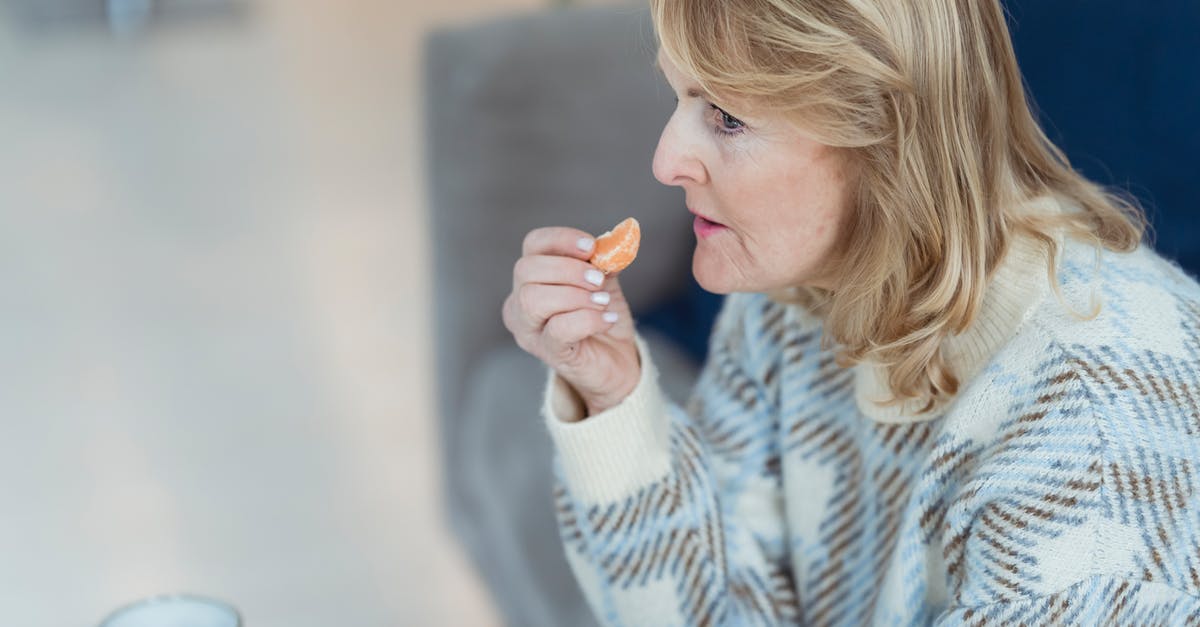 How can I concentrate citrus juice at home? - Side view of mature lady with blond hair in warm sweater eating rip healthy tangerine while drinking tea at table on cozy sofa and looking away