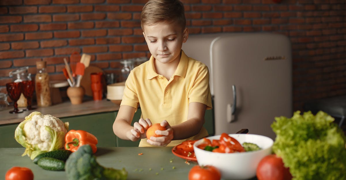 How can I concentrate citrus juice at home? - Confident kid peeling fresh orange sitting at table with assorted vegetables and fruits near salad bowl during vegetarian meal preparation in loft kitchen with brick walls