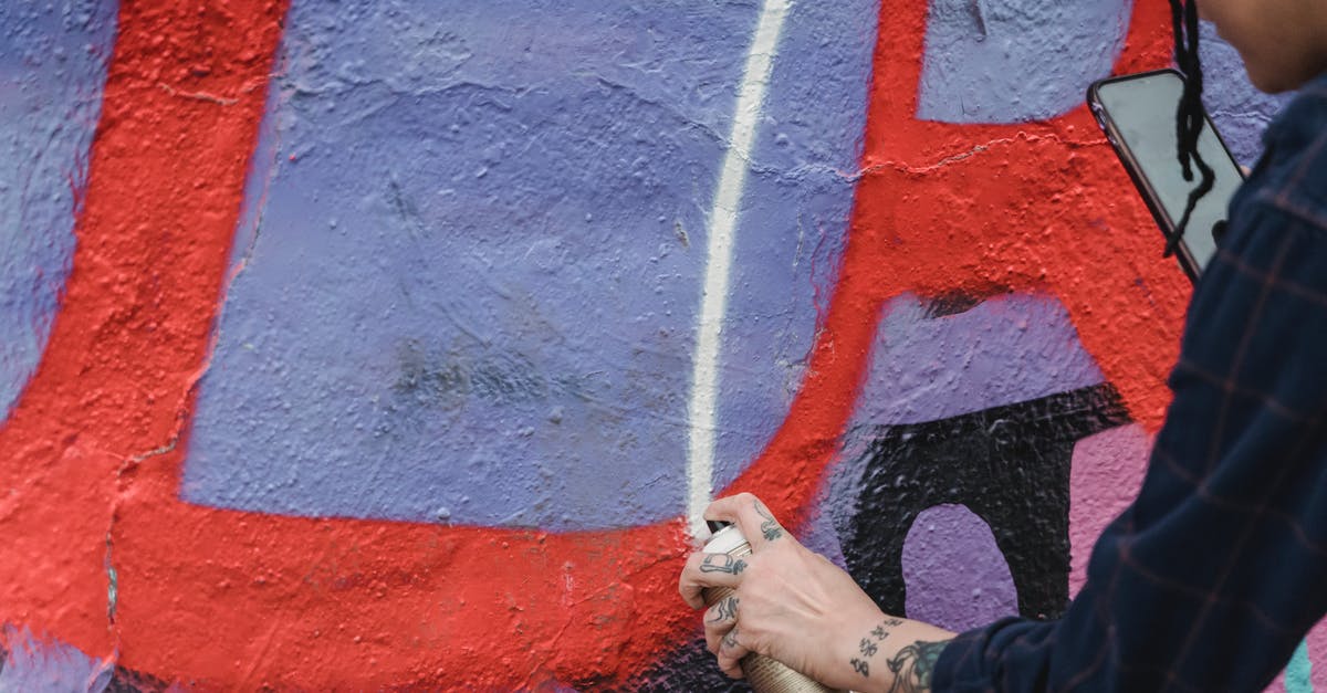 How can I create a drinkable ice slurry? - Side view of crop unrecognizable painter spraying paint on colorful wall with patterns while creating graffiti on street of city