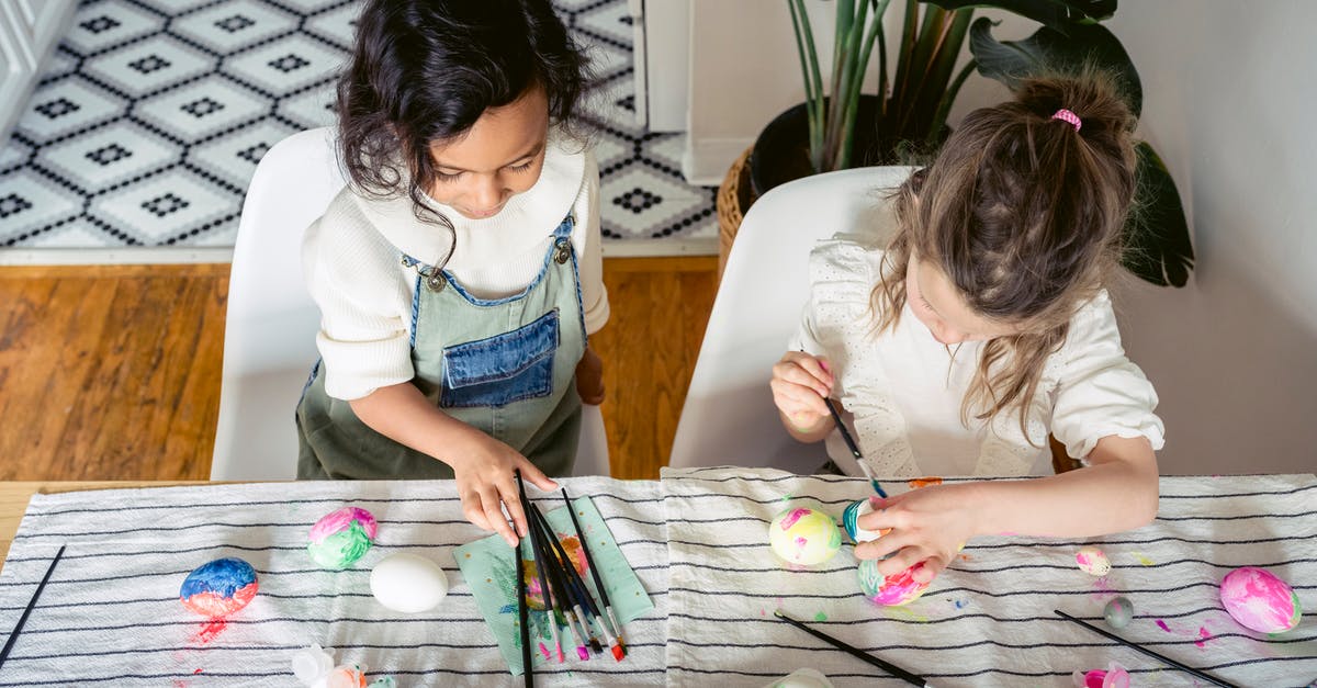 How can I create a scotch egg with a runny yolk? - From above of concentrated multiracial girls painting eggs with paintbrushes while sitting at table with textile during Easter holiday at home