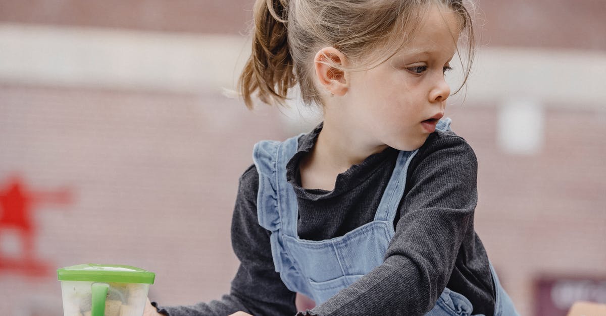 How can I create a sweet pizza that looks like pizza? - Crop cute preschool kid with ponytail in casual clothes sitting at table with colorful stationery for painting and looking away