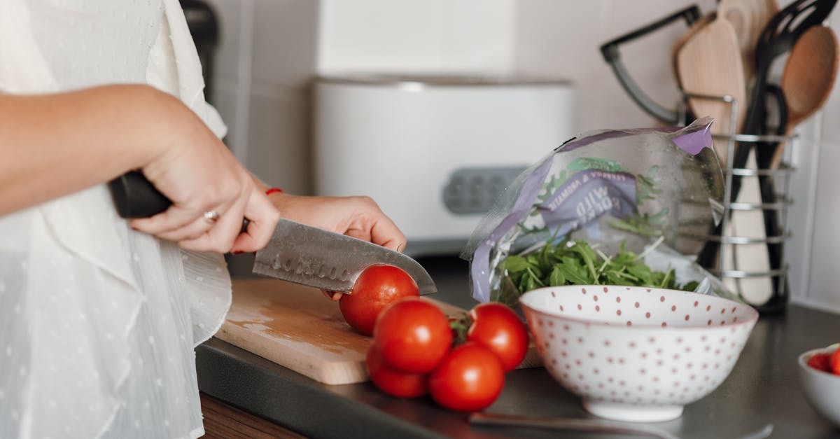 How can I cut a tomato without a knife? - Crop anonymous housewife in casual clothes cutting fresh ripe tomatoes with sharp knife on wooden cutting board while cooking in kitchen