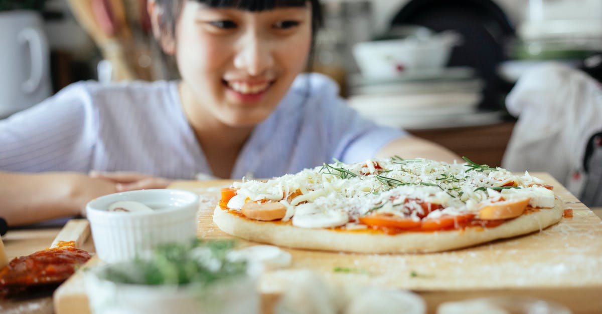 How can I improve my gluten-free pizza dough? - Crop Asian lady smiling and looking at homemade pizza placed on wooden table among various fresh ingredients and utensil in kitchen