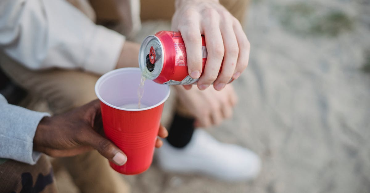 How can I keep my reheated Oats from sticking together? - From above of crop anonymous man pouring fizzy drink from can into red plastic cup of black friend while sitting on sandy ground