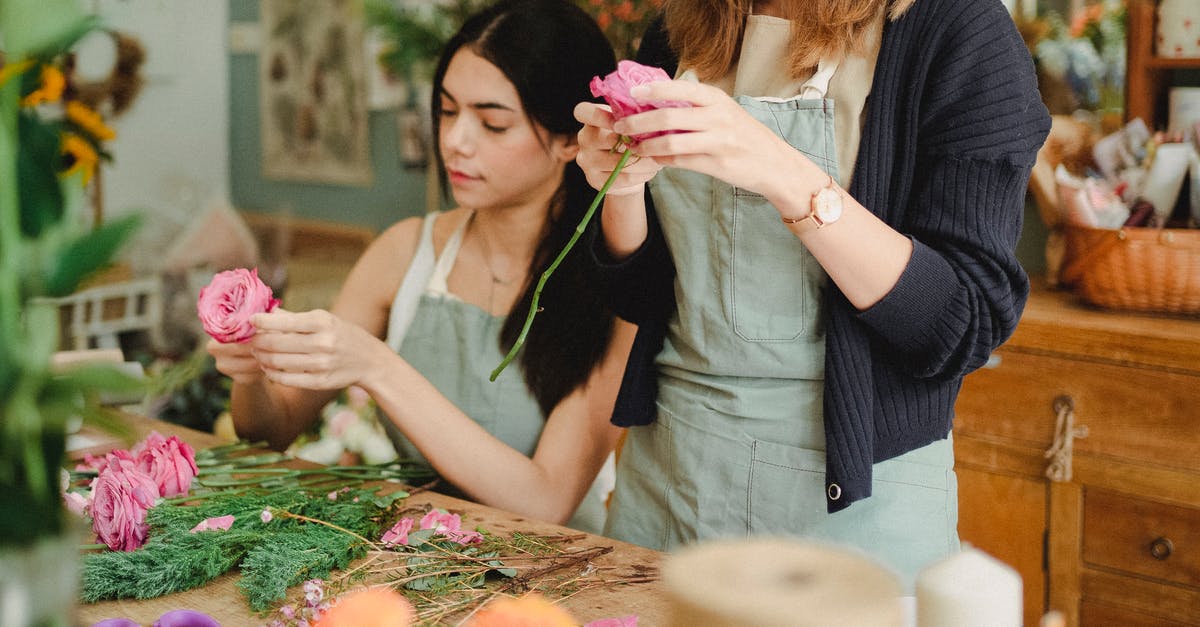 How can I make and store multiple pizzas before a potluck? - Positive young female florists wearing aprons removing leaves from flower stems before arranging bouquet in modern floristry store