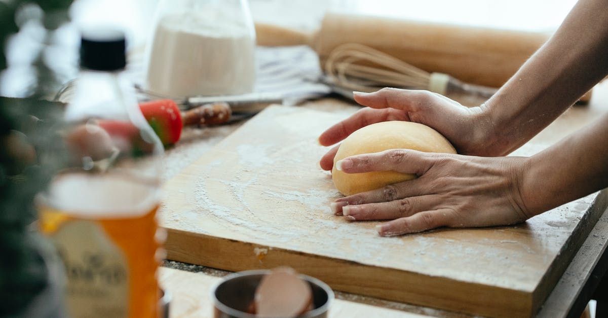 How can I make bacon powder? - Anonymous female cook with ball of raw dough on wooden board standing at table while kitchenware while cooking in kitchen against blurred background