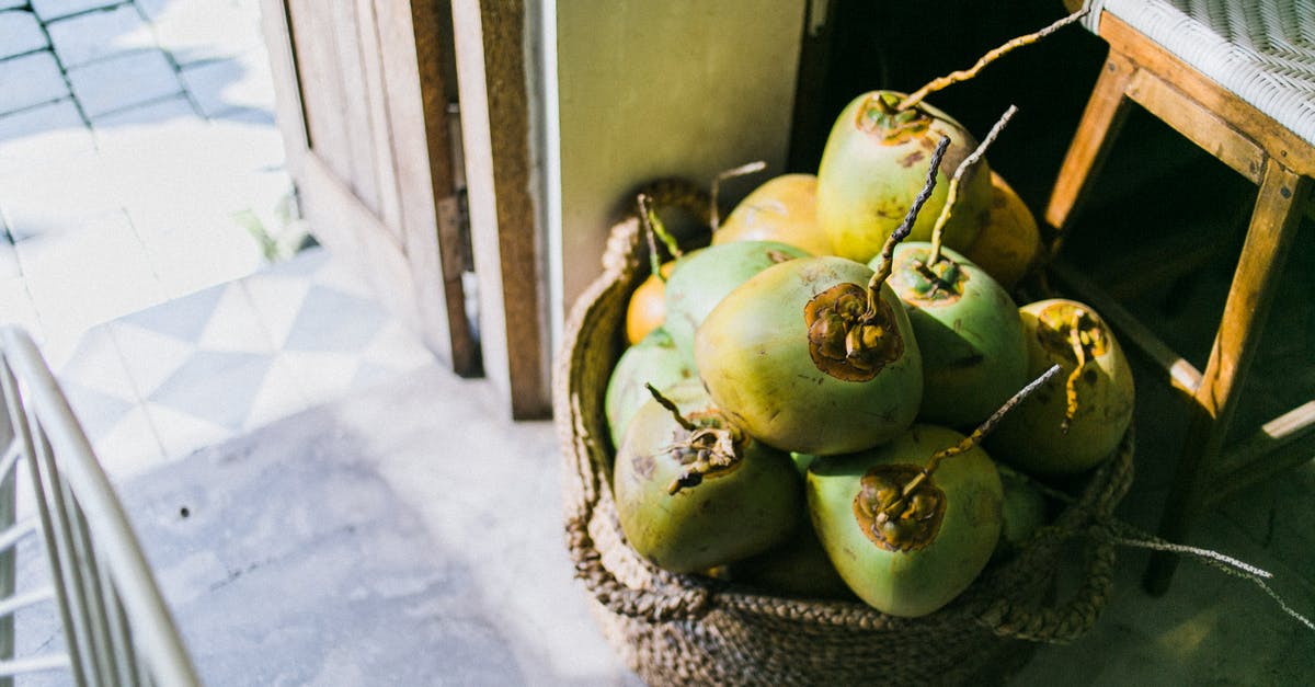 How can I make dry coconut from fresh coconut meat? - From above of young light green coconuts in fabric basket next to old wooden stool in daytime