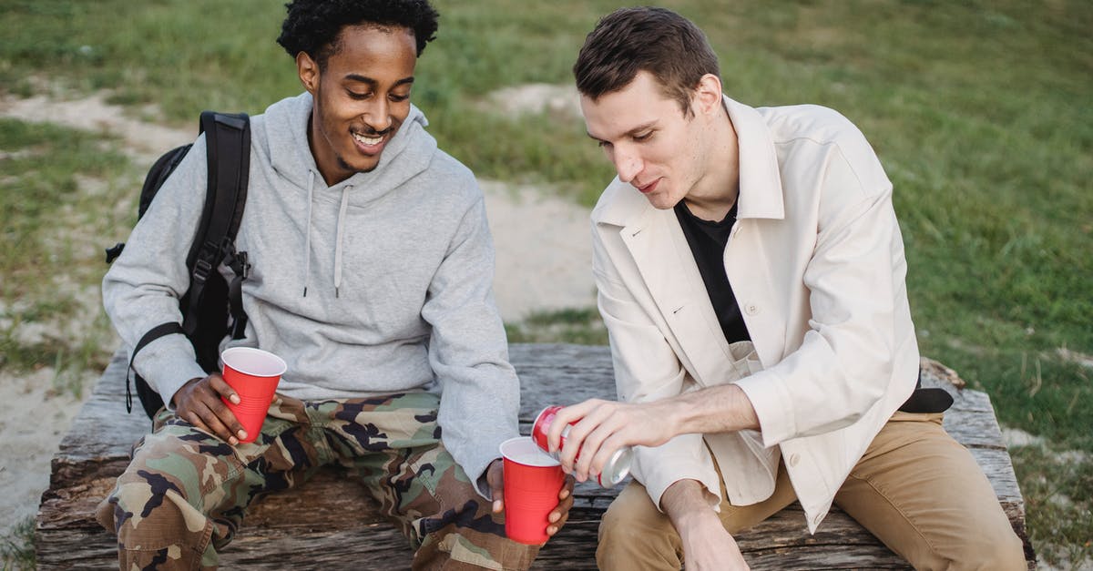 How can I make pierogi gluten-free? - High angle of male pouring carbonated drink from tin can to smiling black friend sitting with red cup