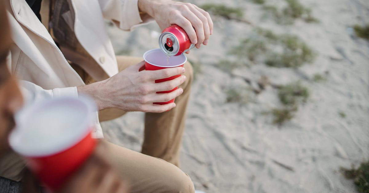 How can I prevent coconut cream from curdling in a soda drink? - High angle of crop anonymous male pouring refreshing drink into red cup while sitting on sandy shore with black friend