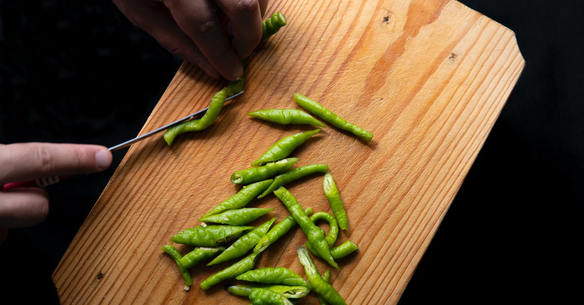 How can I process Hot Pepper without killing the spice (capsaicin)? - Top view of crop anonymous person cutting fresh green chili peppers on wooden chopping board