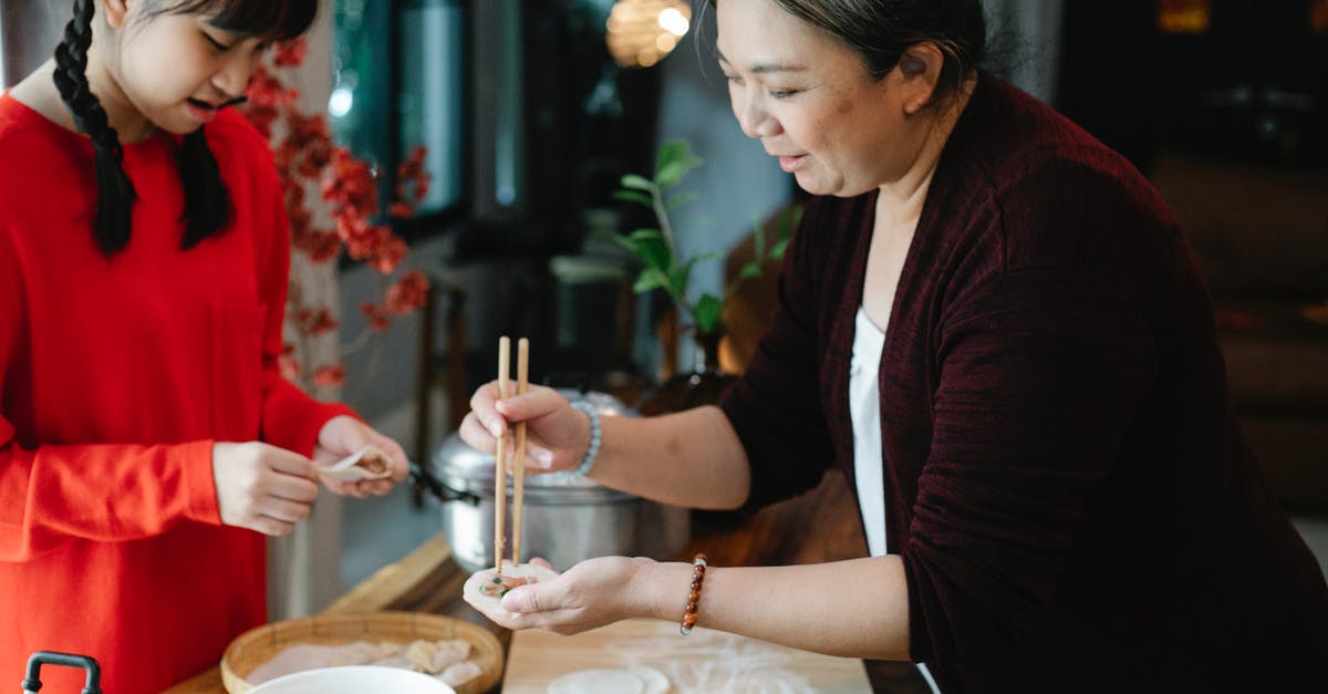 How can I "cheat" on dough maturation? - Crop teenage Asian girl with dark hair helping grandmother to fold traditional Chinese jiaozi dumplings while cooking together in kitchen
