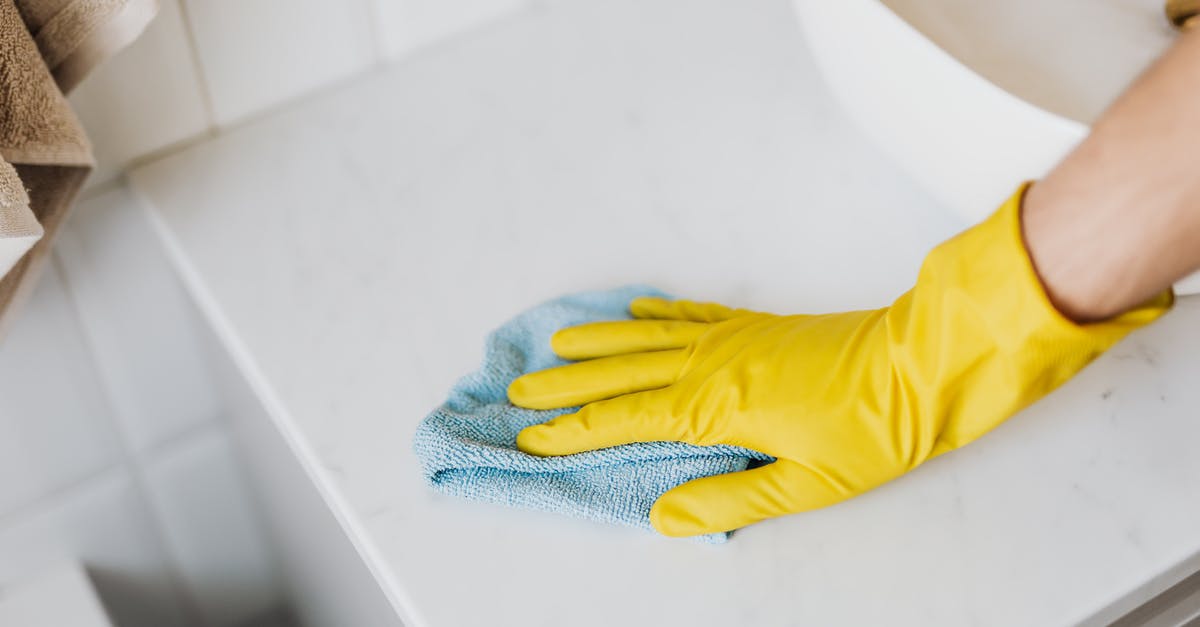 How can I remove burnt smell from white sauce? - From above crop unrecognizable person with microfiber cloth wearing yellow rubber glove and cleaning white marble tabletop of vanity table with washbasin in bathroom