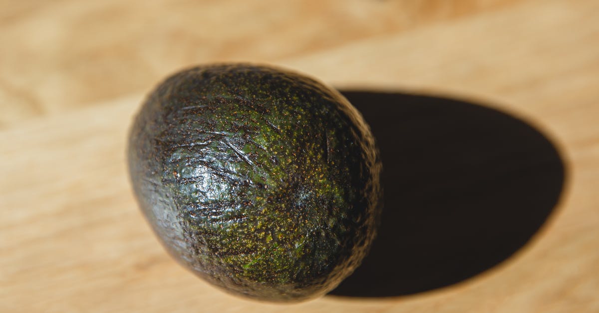 How can I remove the peel and pit of an avocado without the whole thing turning into mush? - High angle of healthy avocado with dark green peel placed on wooden table in daylight