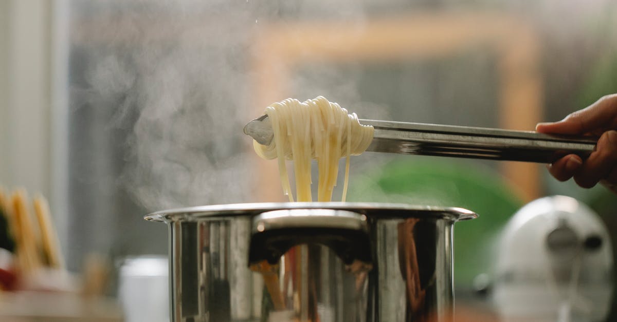 How can I stop fish from sticking to a stainless steel pan? - Low angle of crop anonymous chef taking spaghetti from pan with boiling steaming water
