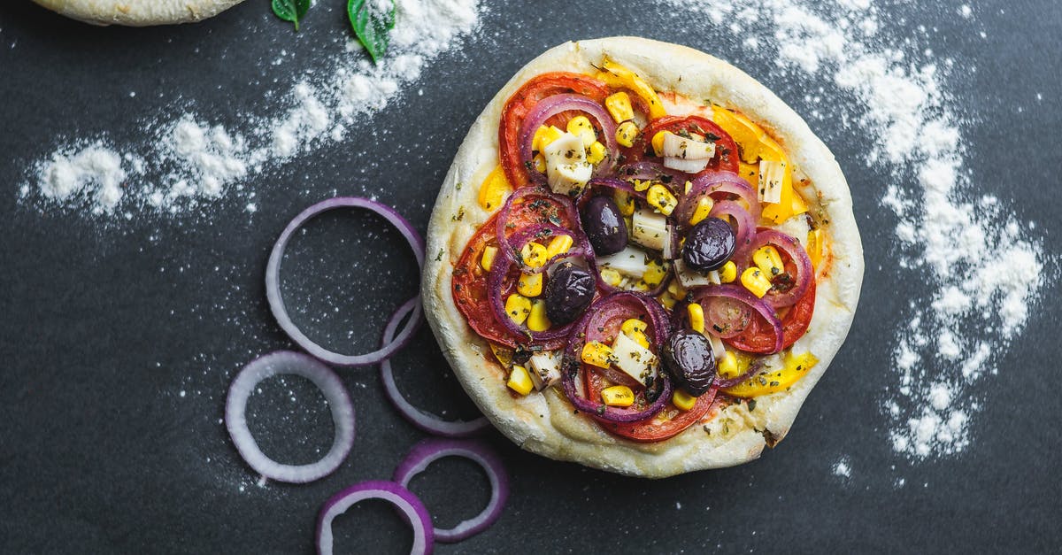 How can I use corn meal more efficiently when making pizzas? - Flat lay of pizza with sliced onion and tomatoes covered with corns on table with flour and green leaves