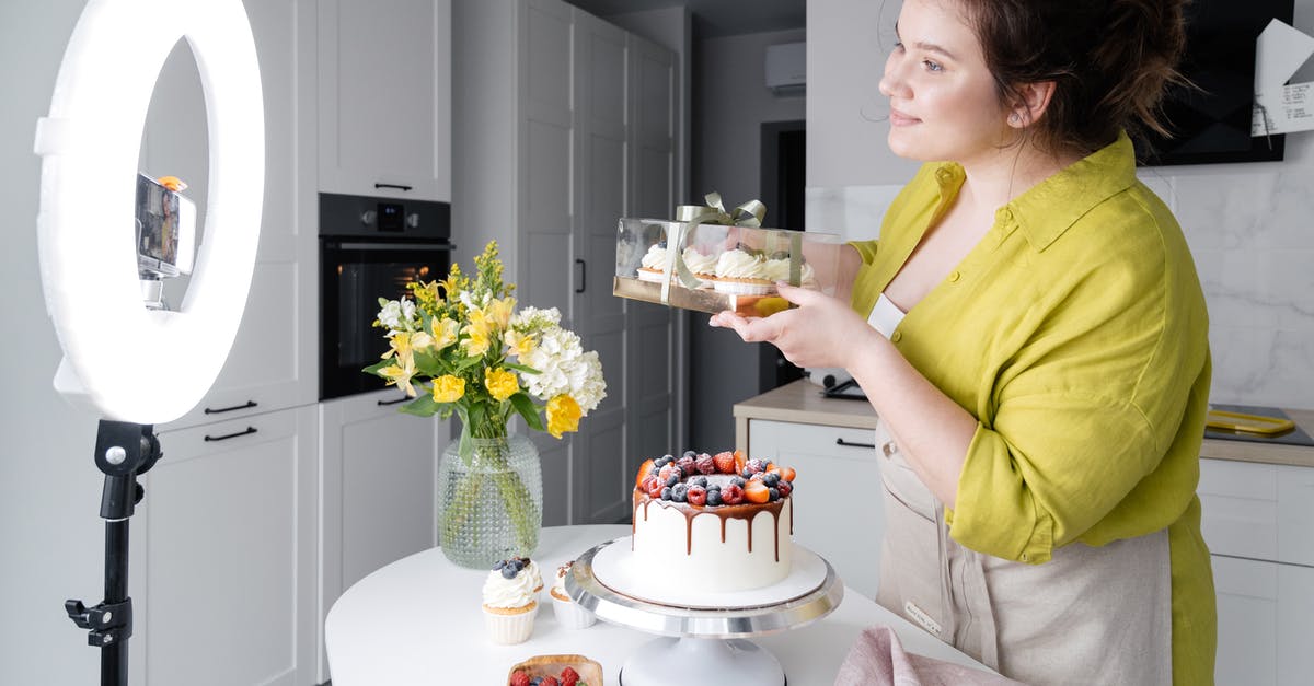 How can I use these peaches in a box cake mix? - Side view of positive young female food blogger in casual clothes and apron introducing yummy cakes and smiling while standing in front of ring lamp and recording vlog on smartphone