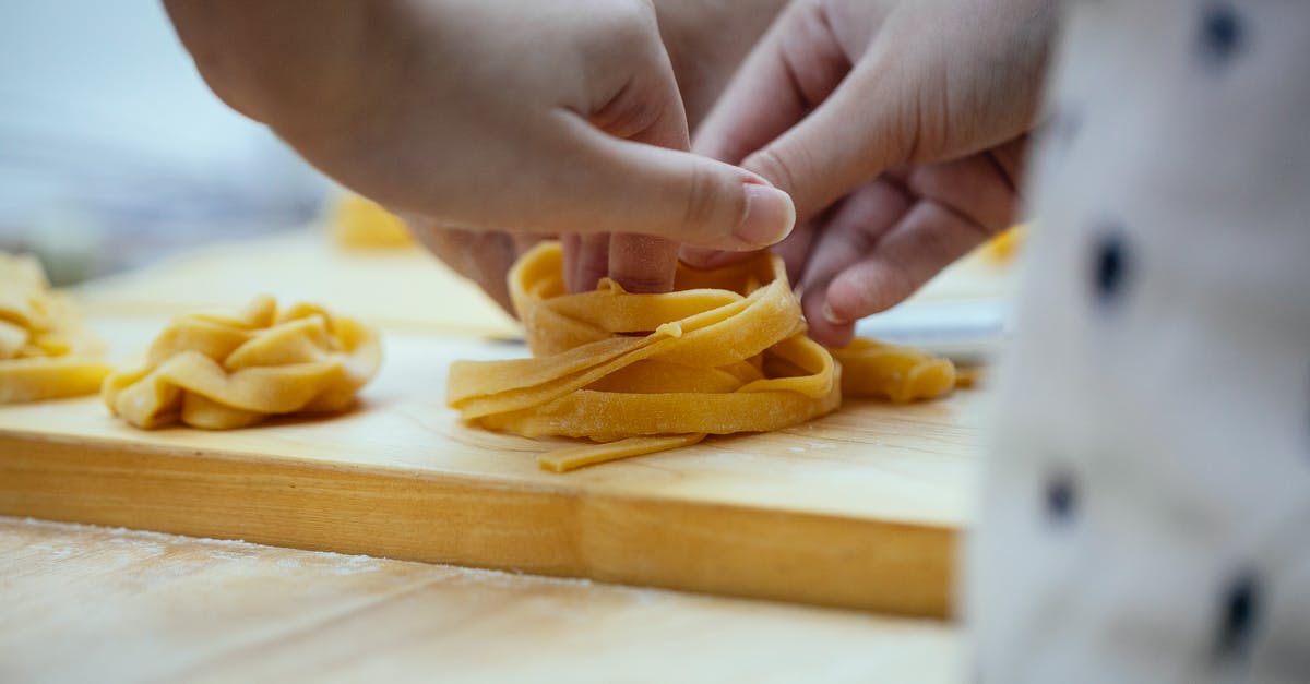 How do chefs come up with recipes for good food? - Crop unrecognizable female cook creating nest from homemade tagliatelle egg pasta placed on wooden cutting board while preparing dinner in kitchen