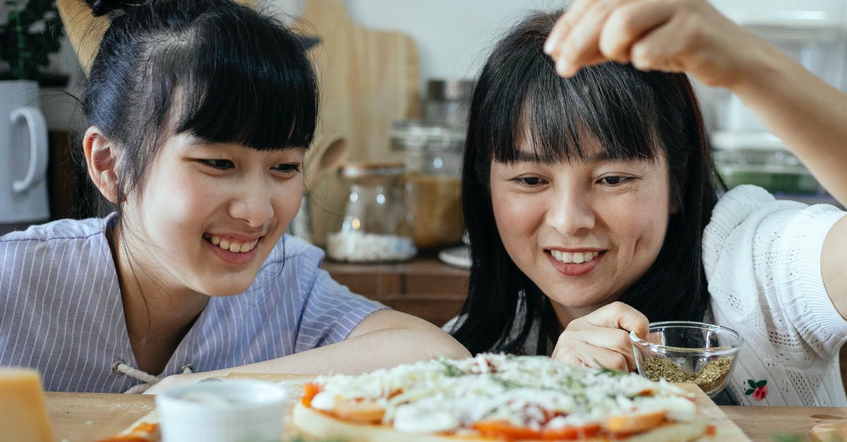 How do I add spice after cooking gravy? - Smiling ethnic women adding condiments on pizza