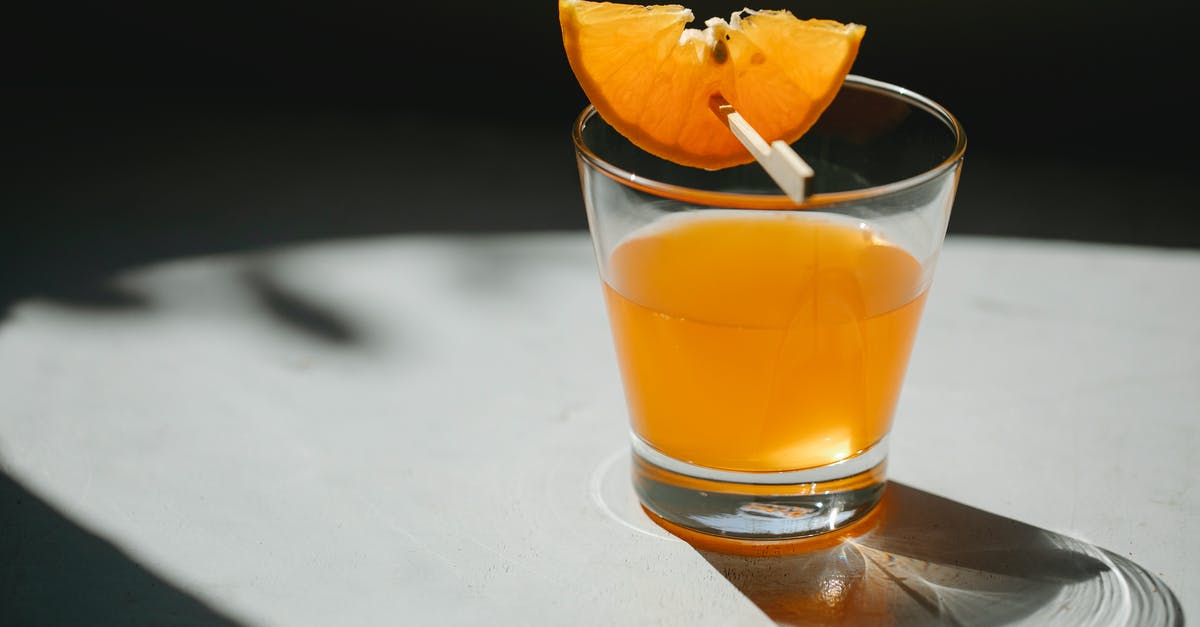 How do I concentrate the flavor in orange juice? - Glass of alcohol drink decorated with slice of orange on wooden stick placed on white table on blurred black background