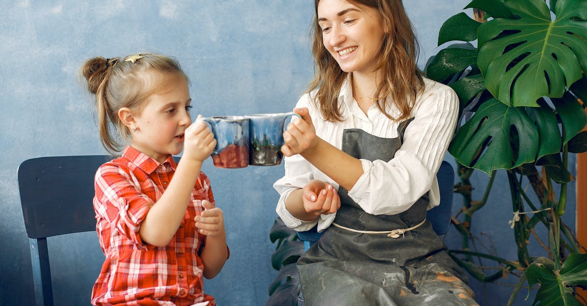 How do I create slippery and light jelly for drinking? - Young smiling female in casual clothes and dirty apron cheering handmade ceramic cups with cute little daughter while sitting together in creative workshop against blue wall