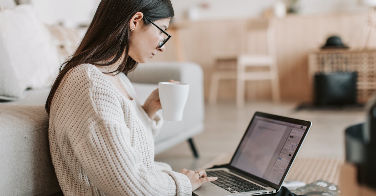 How do I create spherical coffee? - Side view of female freelancer in warm sweater and eyeglasses drinking tea from white ceramic cup while sitting on floor near sofa with netbook on legs while creating document for remote work project