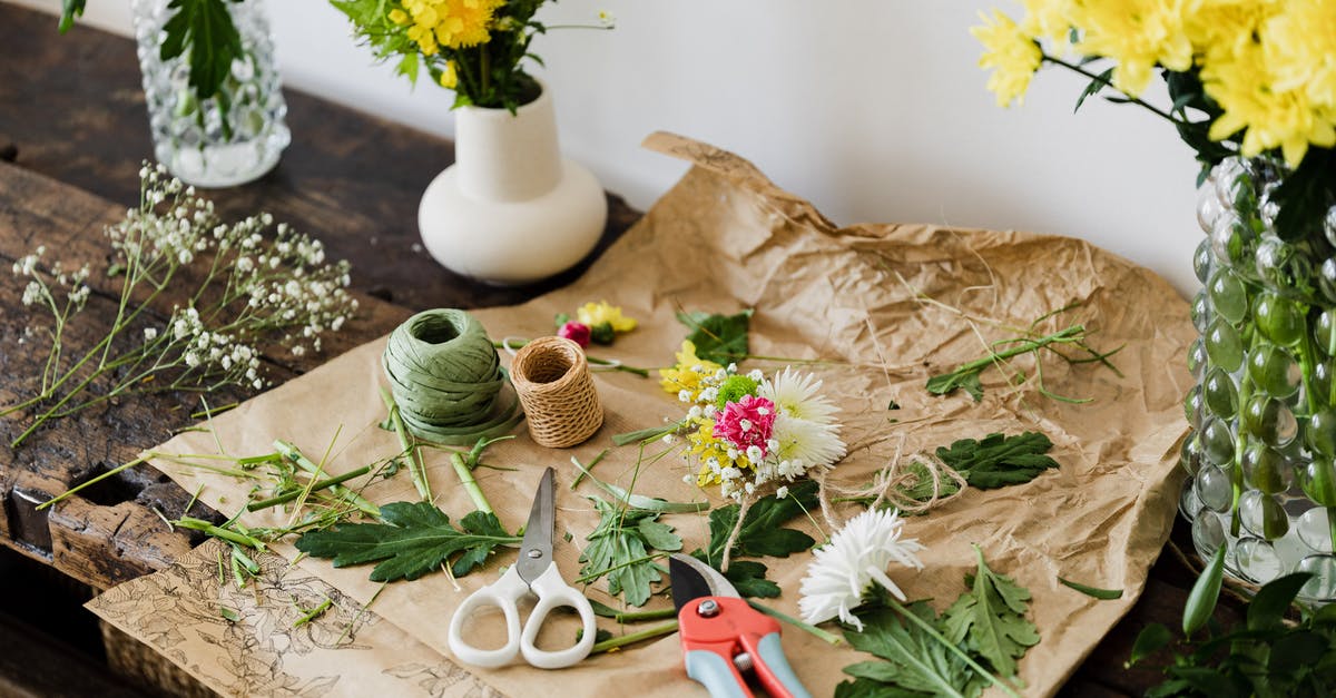 How do I cut a blooming onion? - Scissors and pruner on craft paper covered with cut leaves and flowers among bouquets on wooden table in floristry workshop