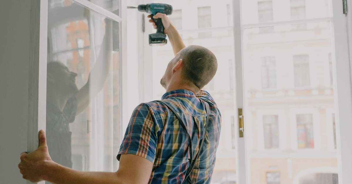 How do I fix my flat sourdough loaf? - Back view of worker in checkered shirt drilling window frame during renovation process in apartment