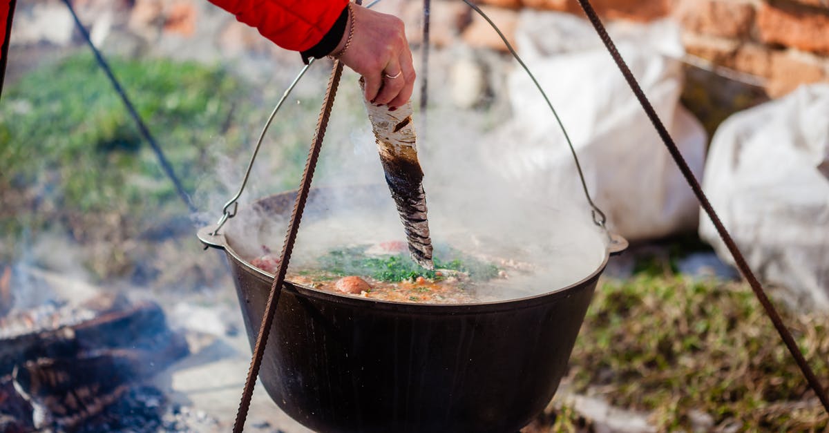 How do I get the burnt aroma off burnt food? - Crop unrecognizable person immersing birch firewood into ukha in cauldron with smoke in daylight on blurred background