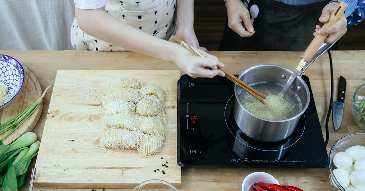 How do I keep the rice cooker from boiling over? - Crop anonymous housewives in aprons boiling noodles on tabletop stove near fresh ingredients in modern kitchen