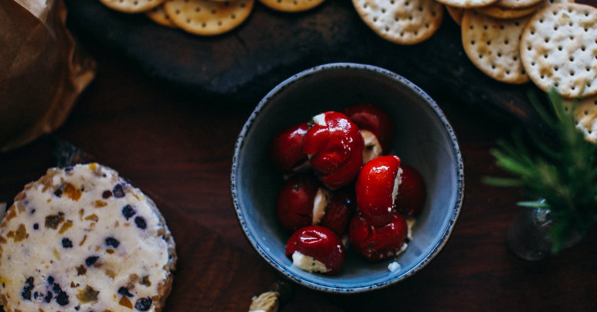 How do I make a cheese, sausage, cracker spread? - Top view bowl with red tiny cherry peppers stuffed with ricotta placed near salty crackers and assorted cheese