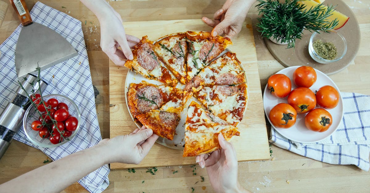 How do I make cumin and herb cheese at home? - From above unrecognizable people taking slices of pizza with salami melted cheese and herbs from plate on kitchen table