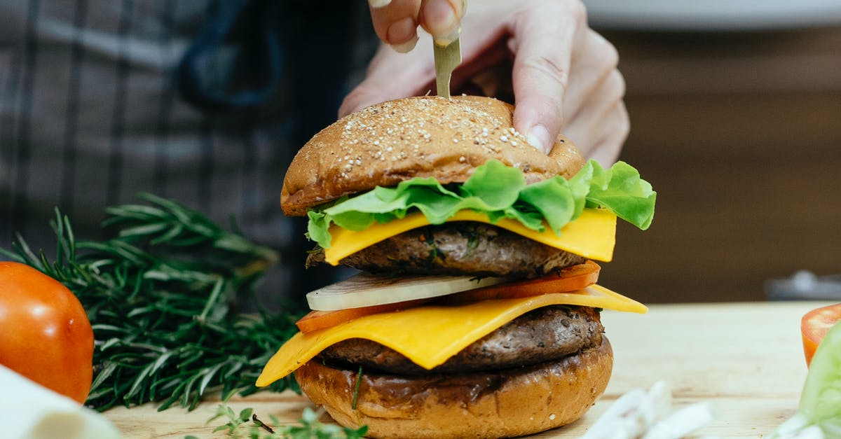 How do I make cumin and herb cheese at home? - Crop unrecognizable female chef inserting skewer into bread bun while preparing delicious cheeseburger between assorted ingredients at home