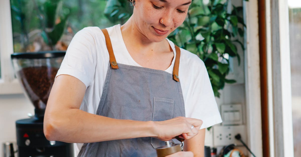 How do I make large spheres using spherification? - Crop happy female in apron smiling and using grinder for preparing aromatic coffee in kitchen