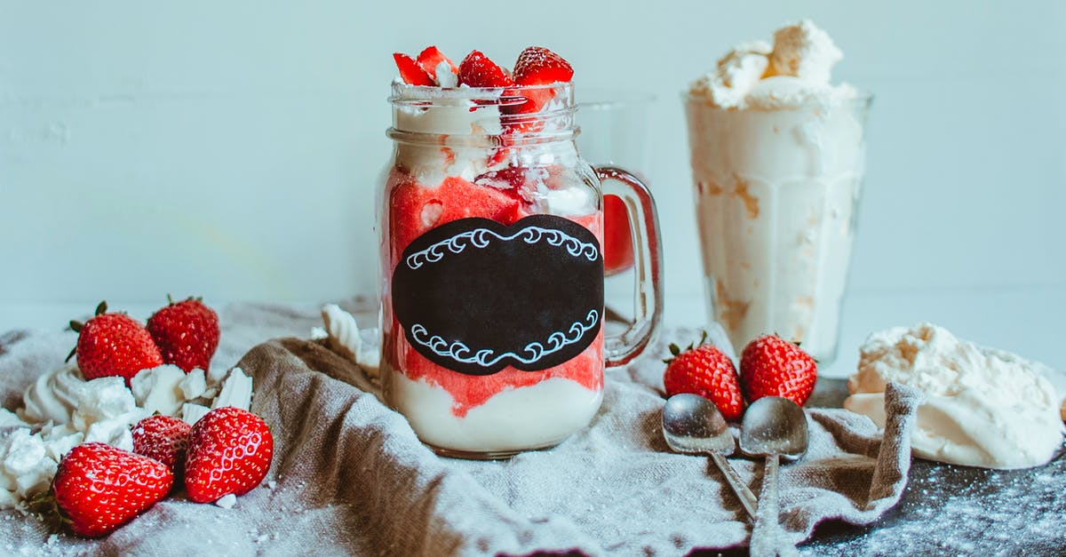 How do I make meringue using a whipped cream charger? - Glass cup with sweet tasty strawberry dessert served with glass of sweet whipped cream and tea spoons on table with napkin and strawberry