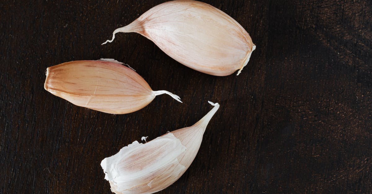 How do I peel garlic in bulk? [duplicate] - Top view of several cloves of ripe garlic in peel placed on wooden desk during cooking process at home