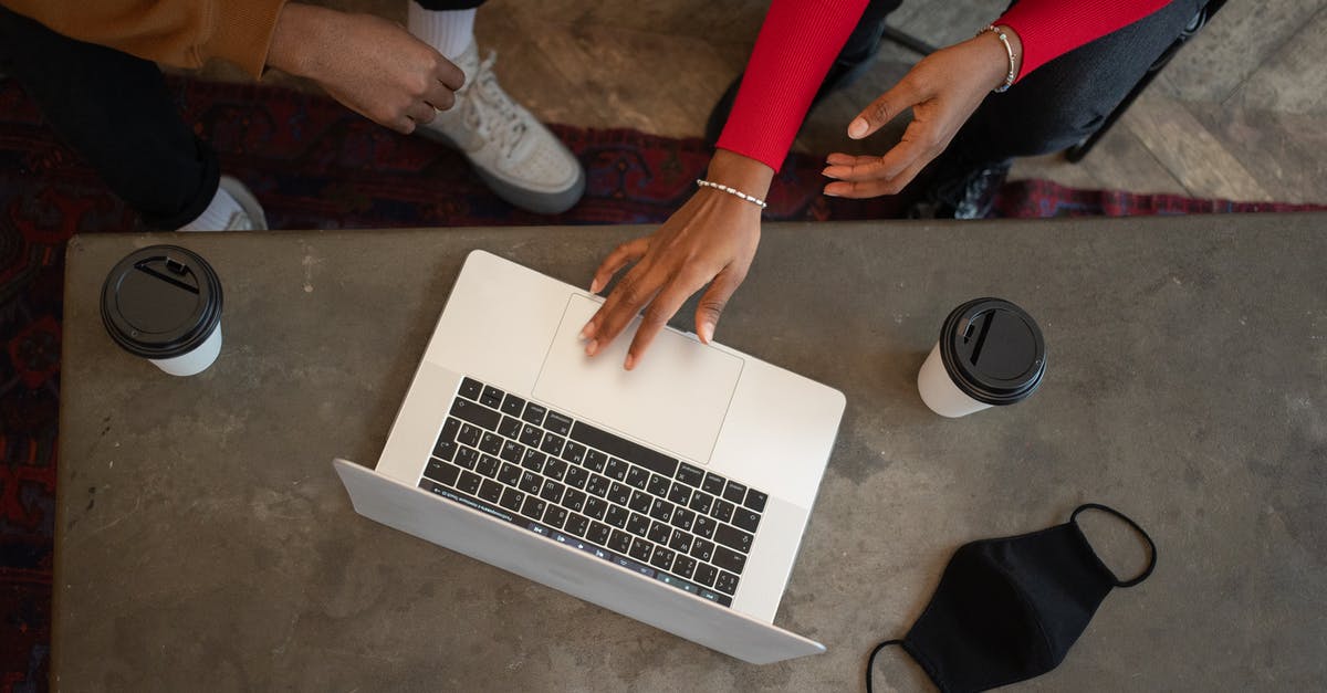 How do I prevent opened canned tuna from going stale? - Top view of crop anonymous African American coworkers surfing netbook while sitting at table with medical mask and takeaway cups of coffee during work