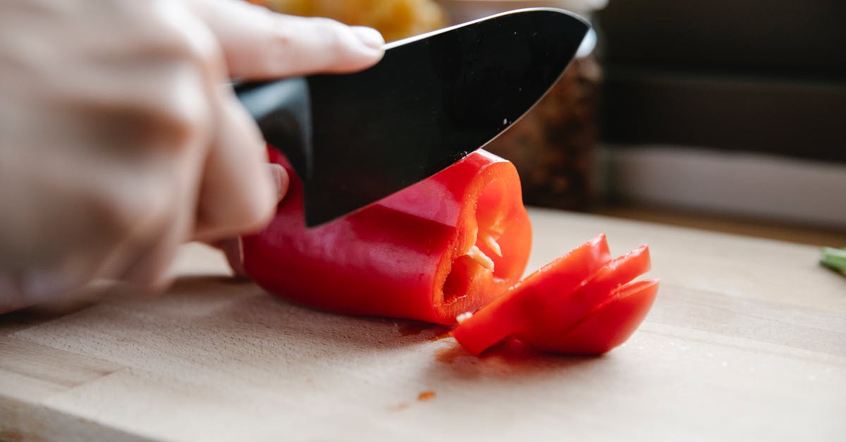 How do I properly cut a bell pepper into a medium dice? - Crop faceless chef cutting ripe red bell pepper on chopping board in light kitchen