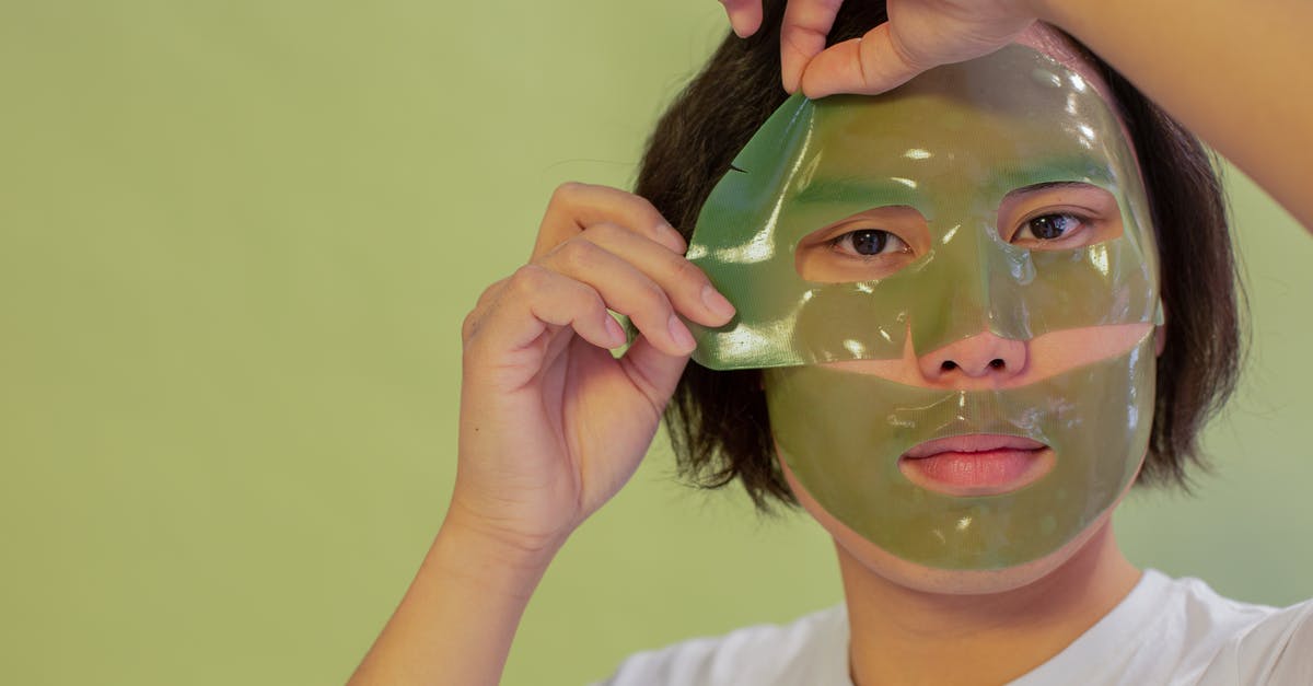 How do I remove a sheet cake from a pan? - Young unemotional Asian male in white shirt removing cleansing mask sheet from face and looking at camera against green background