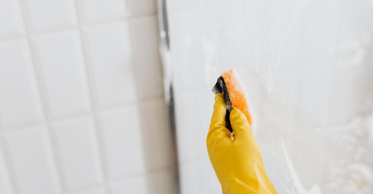 how do I remove partially-disintegrated sediment/tiny-bones from stock? - From above of crop anonymous person in yellow rubber protective glove washing shower cabin glass with sponge and detergent