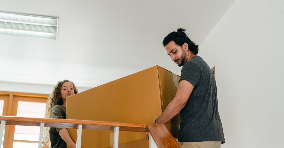 how do I remove partially-disintegrated sediment/tiny-bones from stock? - From below of couple in casual clothes carrying big carton box together while moving packed personal items into new apartment