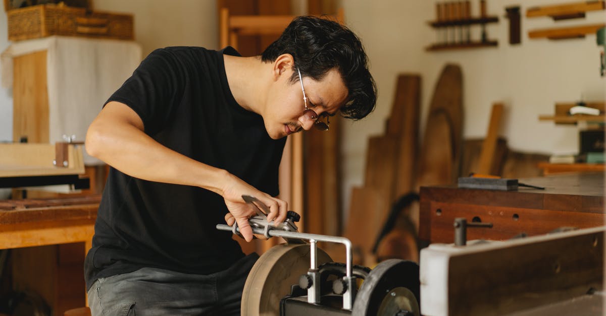 how do I sharpen grinder blade - Young attentive ethnic male joiner in eyewear sharpening manual instrument on grinder with wheels in light workroom